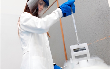 Female lab worker wearing cryogenic personal protective equipment and removing samples from a cryogenic vessel