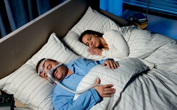 Patient with CPAP mask is sleeping soundly next to his wife in the bedroom.